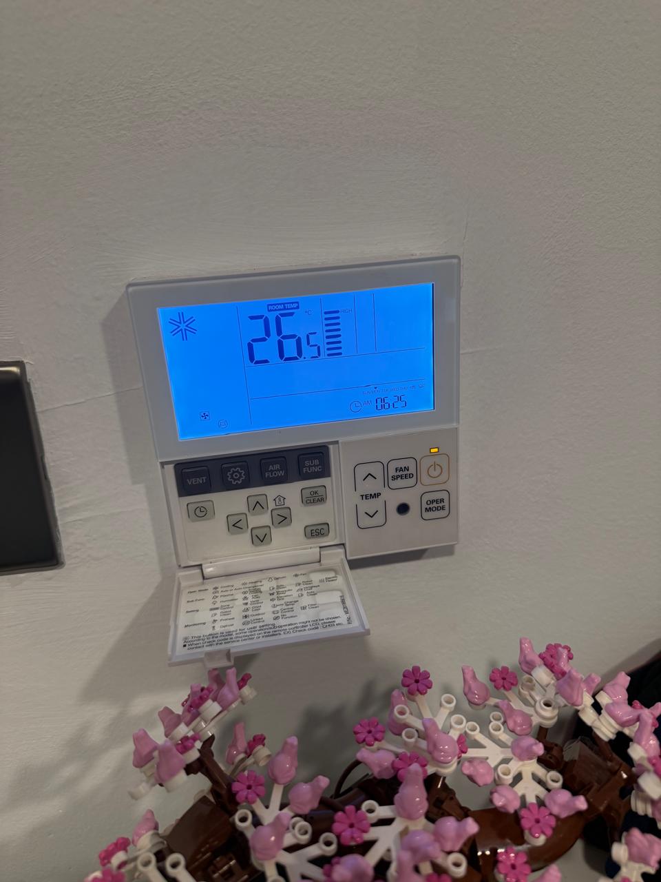 Wall mounted air conditioning controller displaying room temperature and fan settings after commissioning
